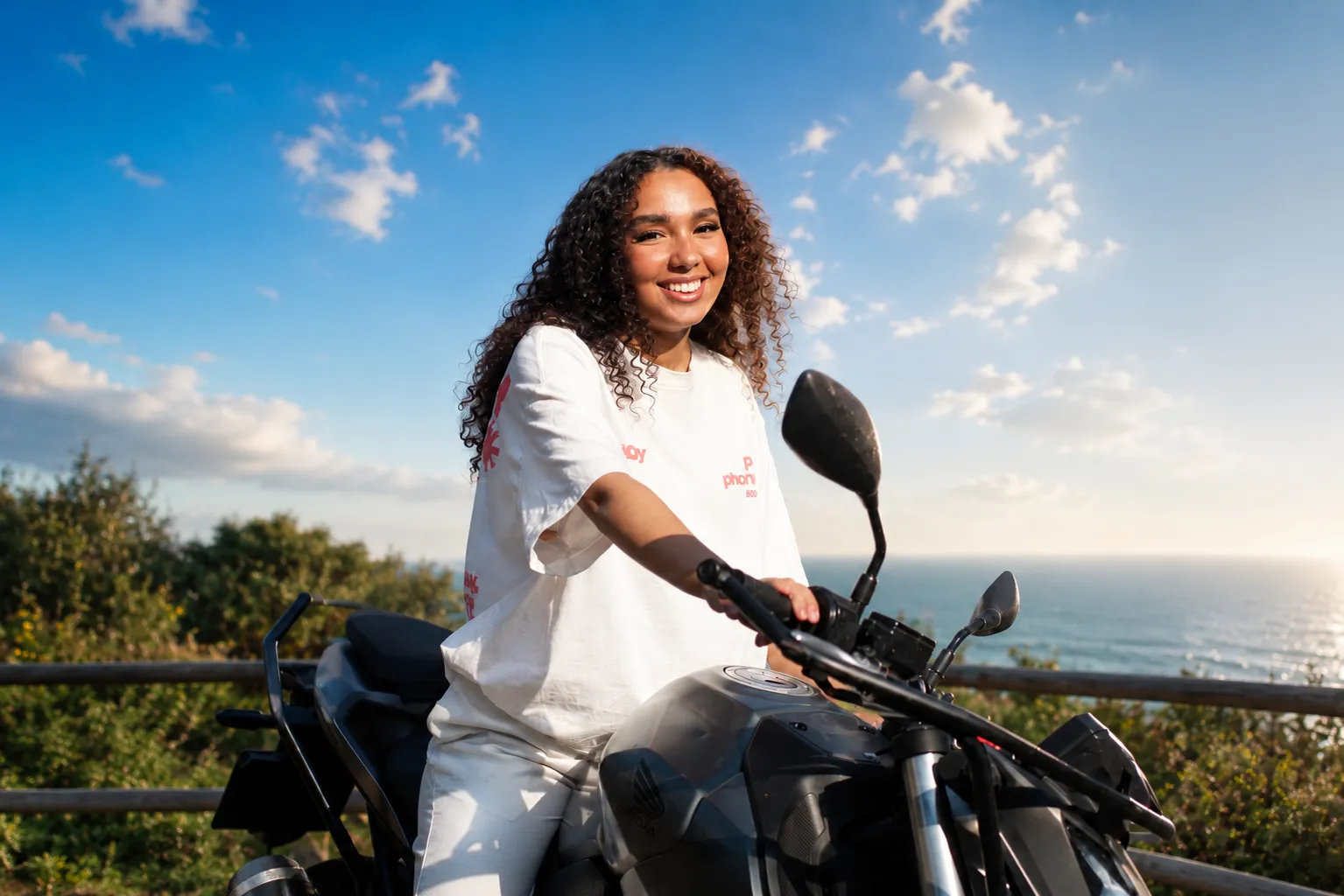 Jeune conductrice souriante sur sa moto au bord de la mer — permis moto WorldofBiz